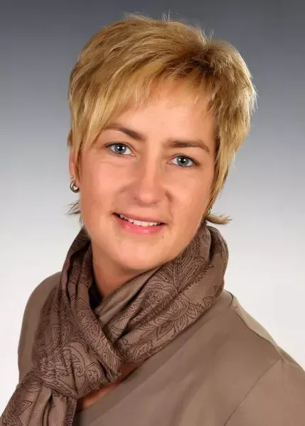 Eine Frau mit einem Schal um den Hals lächelt in die Kamera.