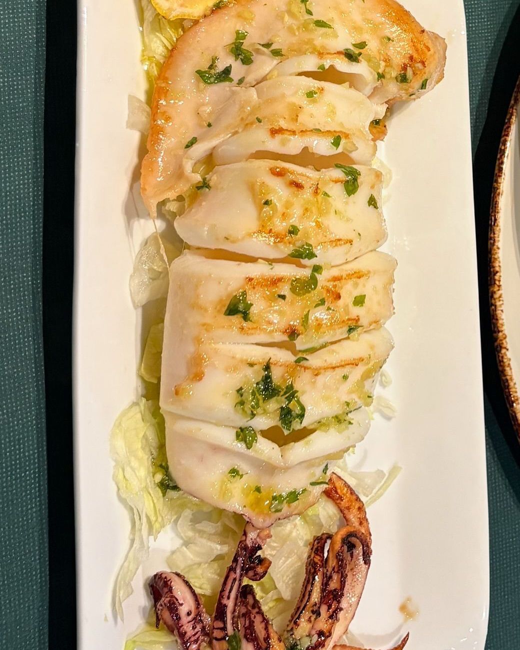 Plato de calamares a la plancha en plato blanco con lechuga, tentáculos visibles.
