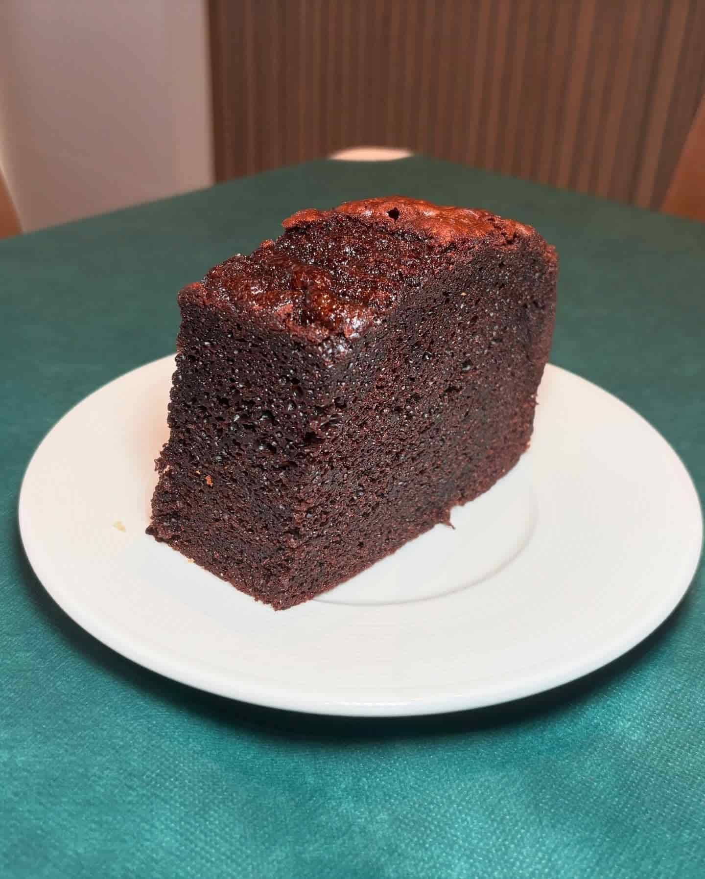 Rebanada de pastel de chocolate negro en un plato blanco, colocado sobre un mantel verde.