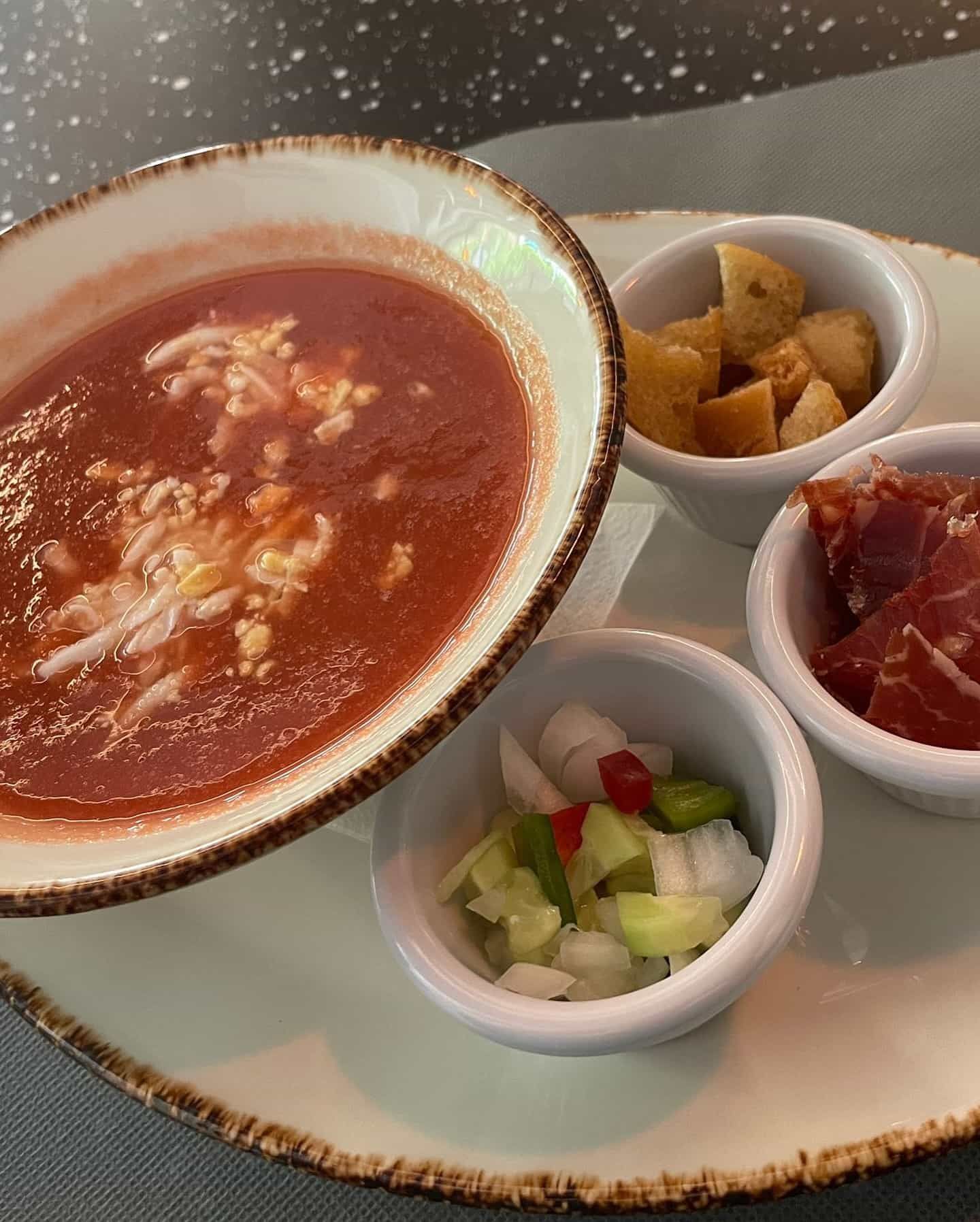Sopa de gazpacho de tomate con picatostes, jamón y verduras picadas.