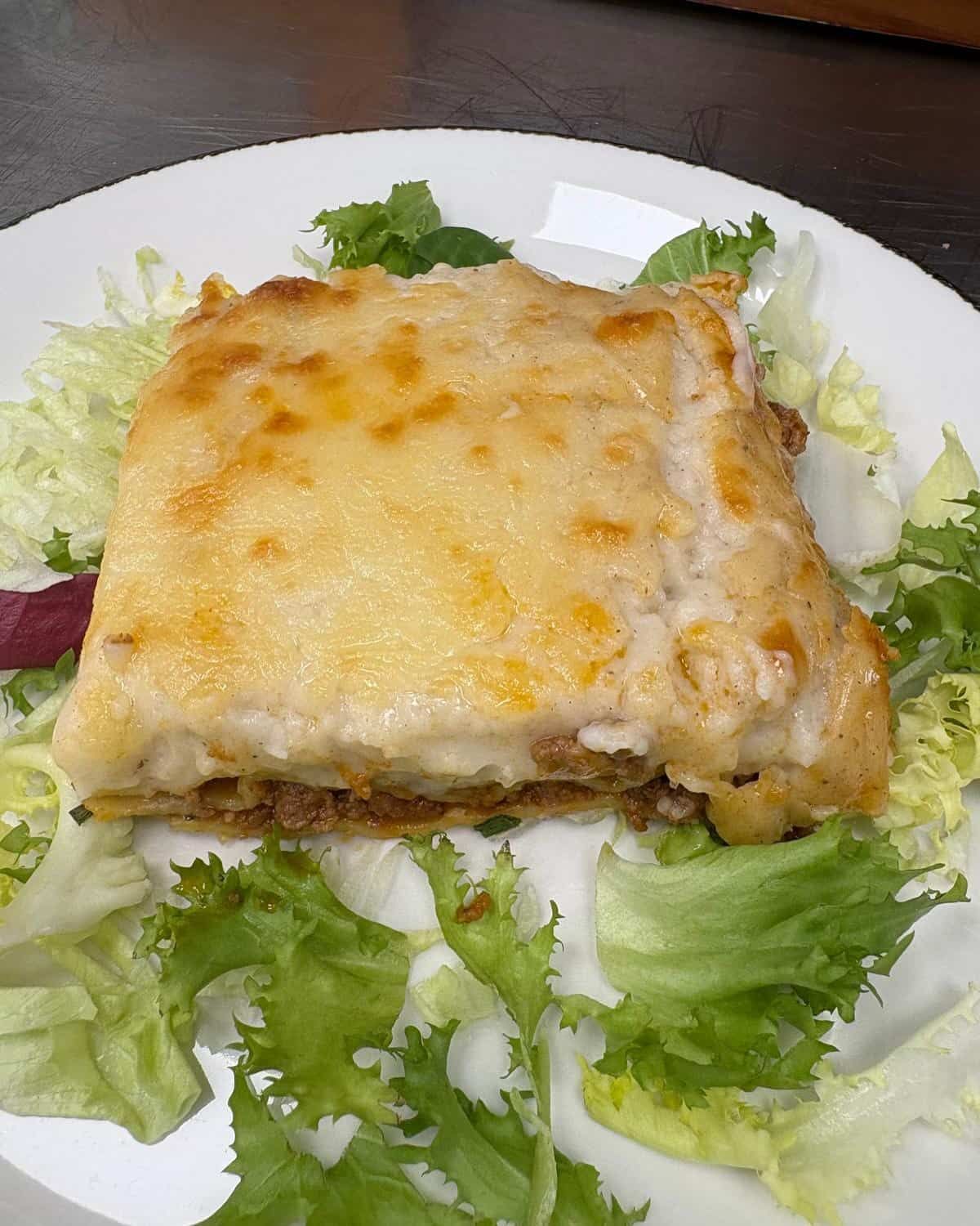 Lasaña en un plato blanco sobre lechuga. Cubierta de queso, capas visibles.