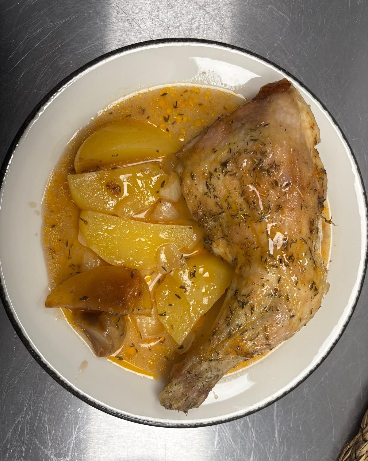 Muslo de pollo con patatas en salsa en un plato blanco.