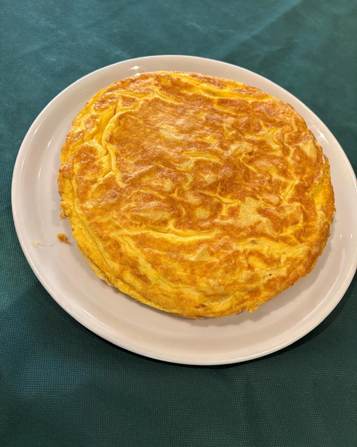 Tortilla Española en un plato blanco, colocado sobre un mantel verde.