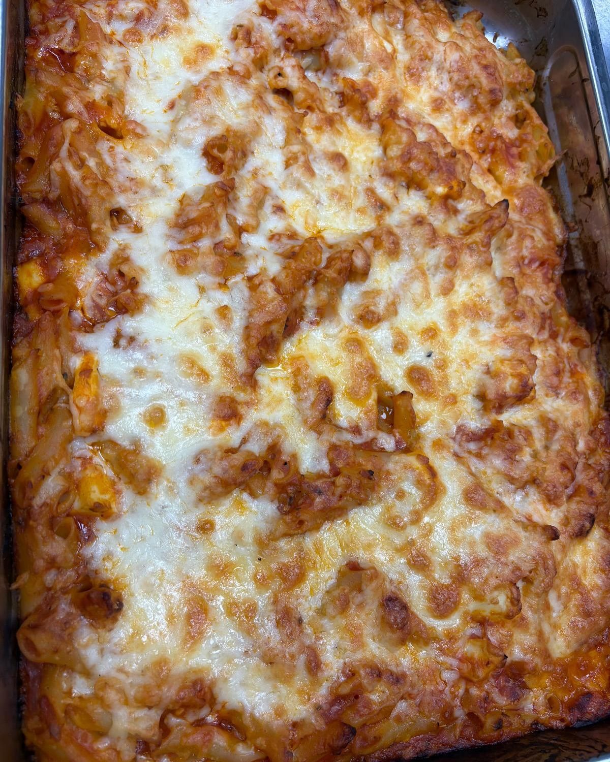 Plato de pasta horneado en una sartén de metal, cubierto con queso blanco derretido y una salsa roja.
