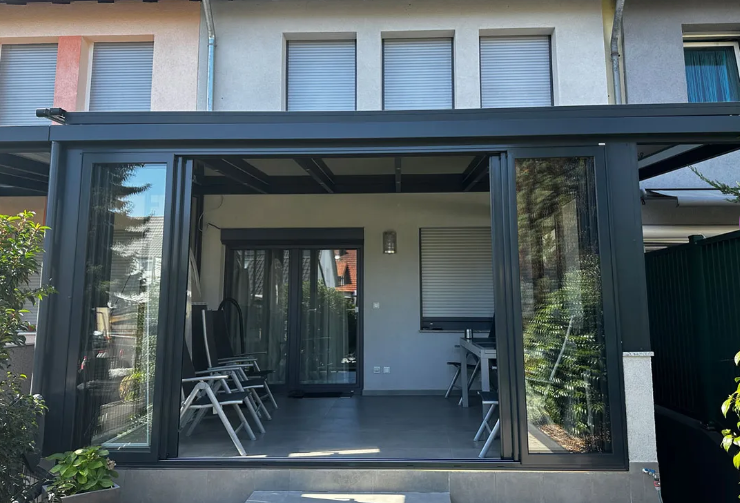 Überdachte Terrasse mit Glasschiebetüren, Stühlen und Topfpflanzen neben einem modernen Haus