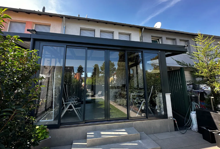 Moderner, verglaster Wintergarten an einem Haus, mit großen Schiebetüren und Treppe davor