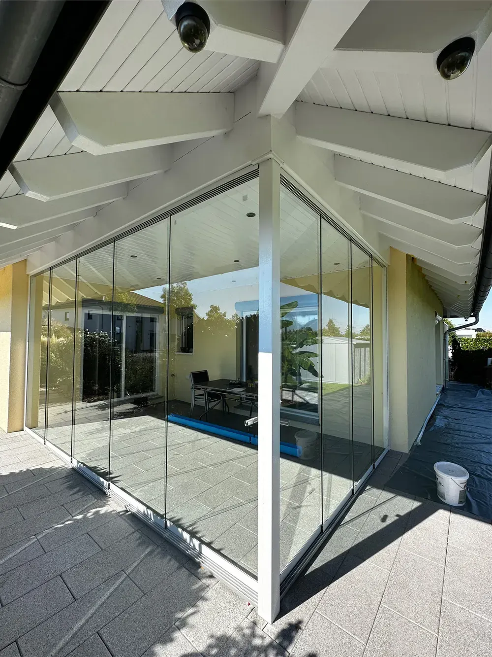 Moderne Terrasse mit Glaswänden, weißen Dachbalken und blauem Poolwasser innerhalb eines überdachten Wohnbereichs im Freien