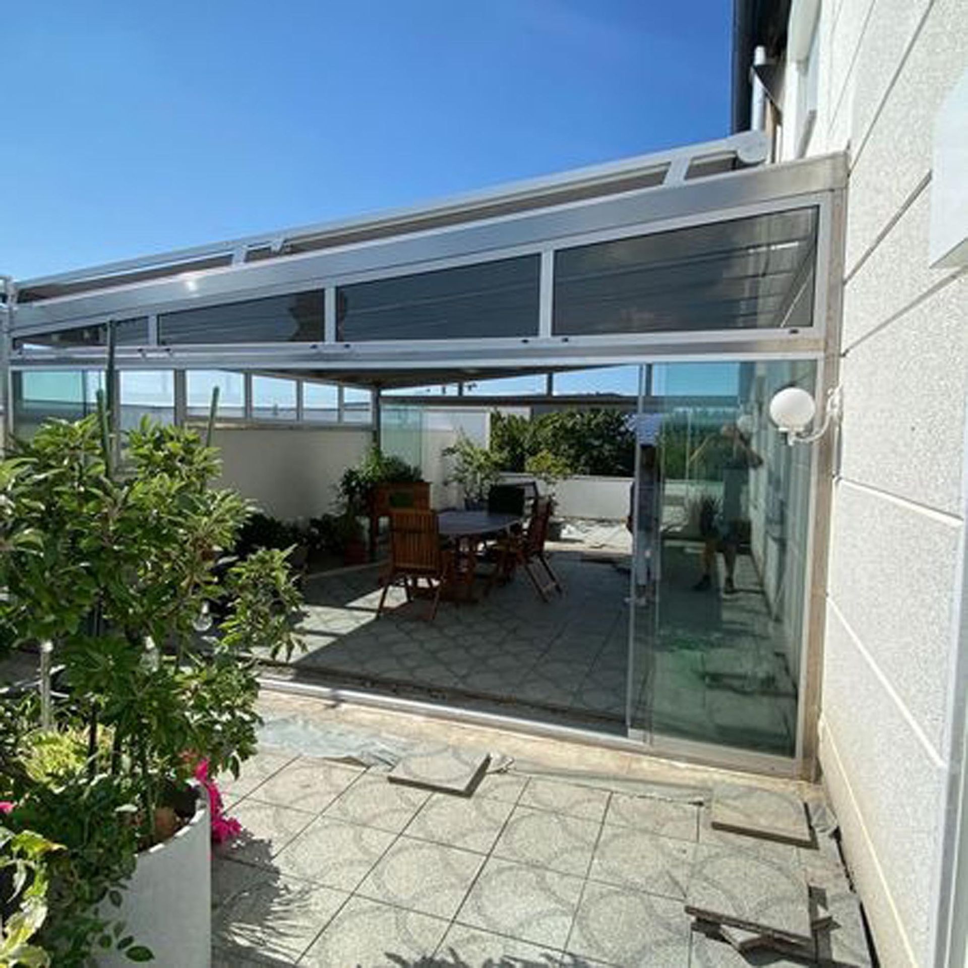 Terrasse mit Glasschiebetüren, Esstisch und Stühlen im Freien, Topfpflanzen und überdachtem Dach