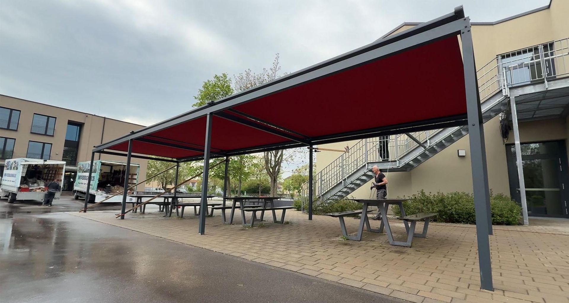 Ein Außenhof mit roten Pavillons, Picknicktischen und nassem Pflaster neben einem Gebäude