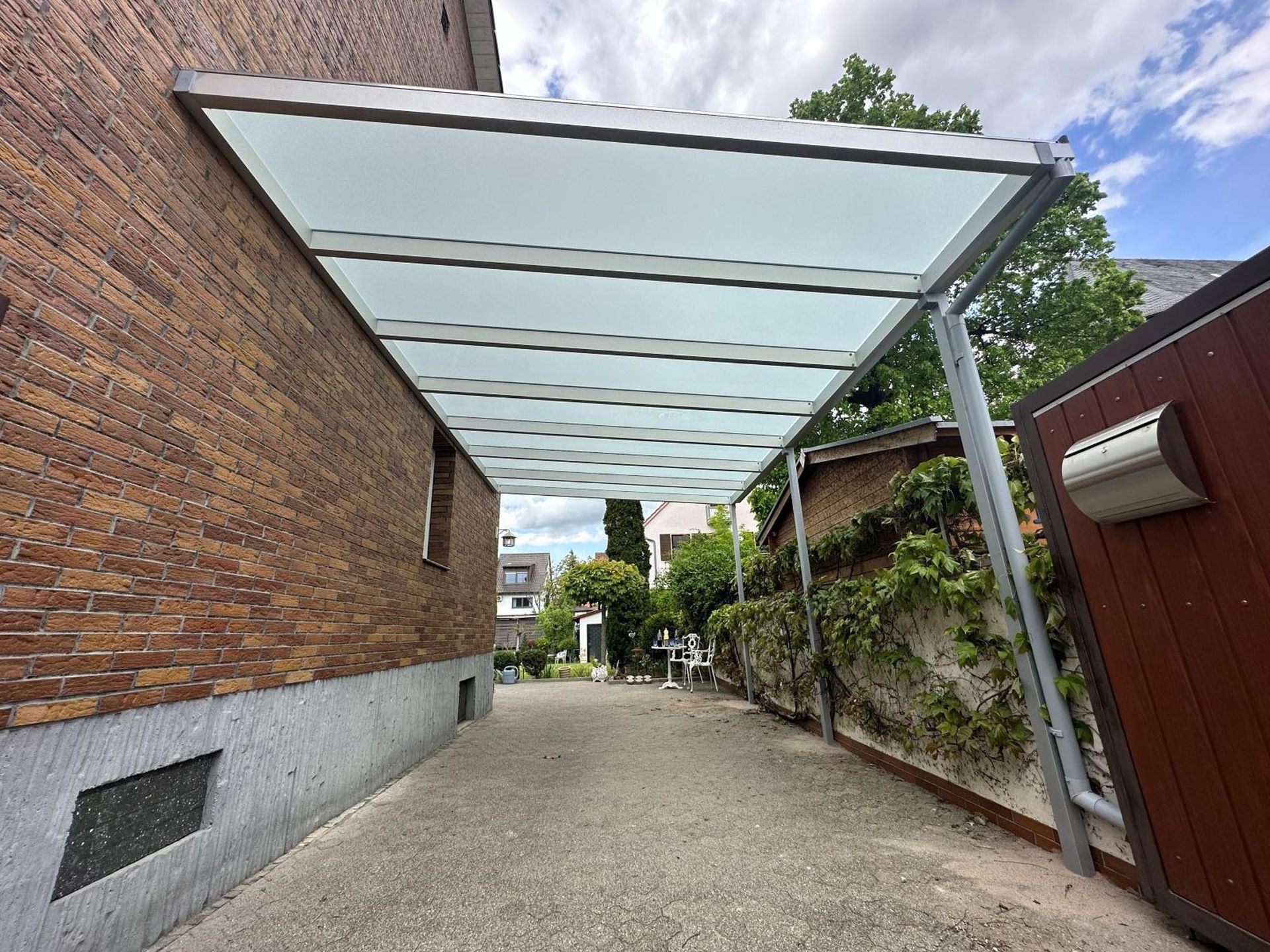 Überdachter Außenweg neben Backstein- und roten Mauern, mit lichtdurchlässigem Dach und Kiesweg.