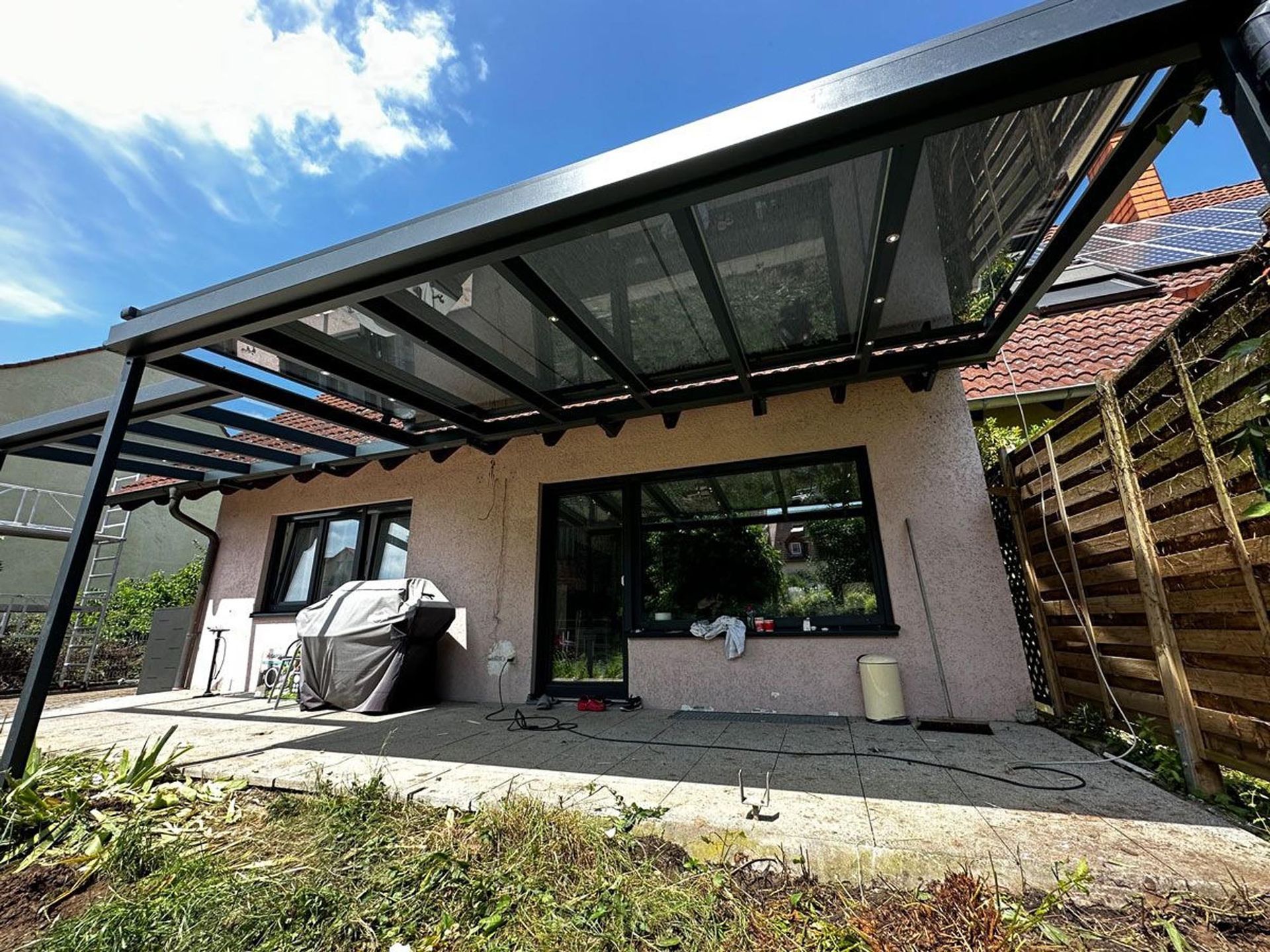 Moderne Terrasse mit schwarzem Metalldach neben einem Haus, Steinpflasterung und überdachtem Sitzbereich im Freien