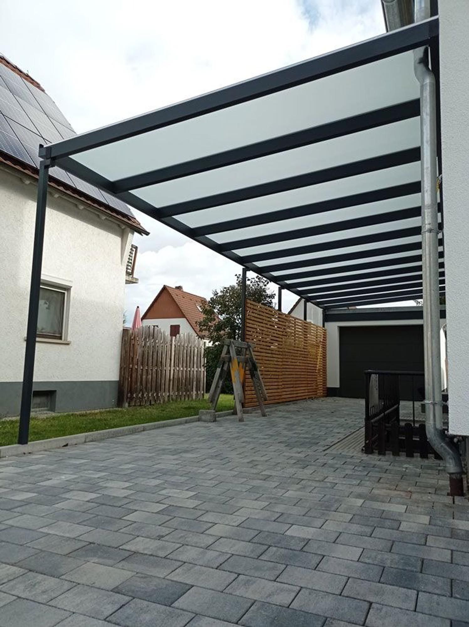 Überdachte Auffahrt mit grauen Pflastersteinen, ein Pergola-Dach aus Metall und eine kleine Auffahrt zur Garage.