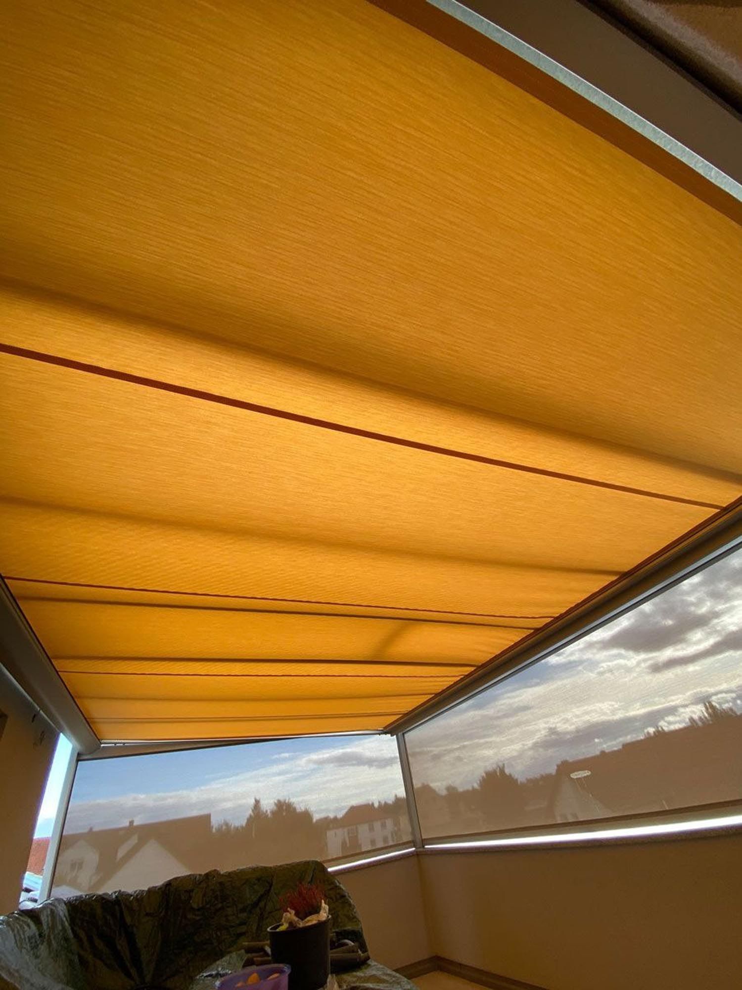 Orangefarbene Markise über einer Terrasse, im Hintergrund bewölkter Himmel.