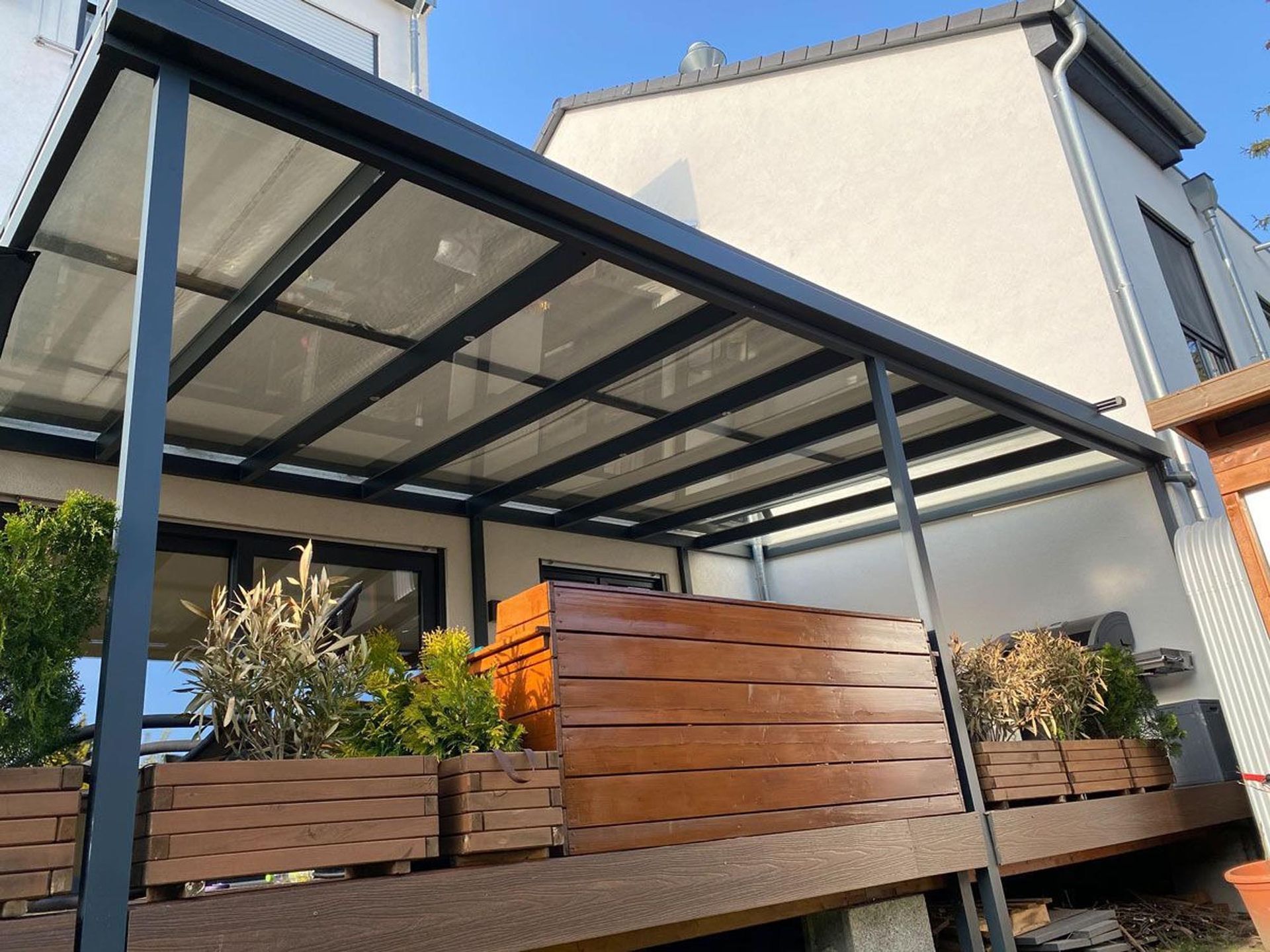 Überdachte Terrasse mit Holzpflanzkästen und einem Lamellendach aus Metall neben einem Haus