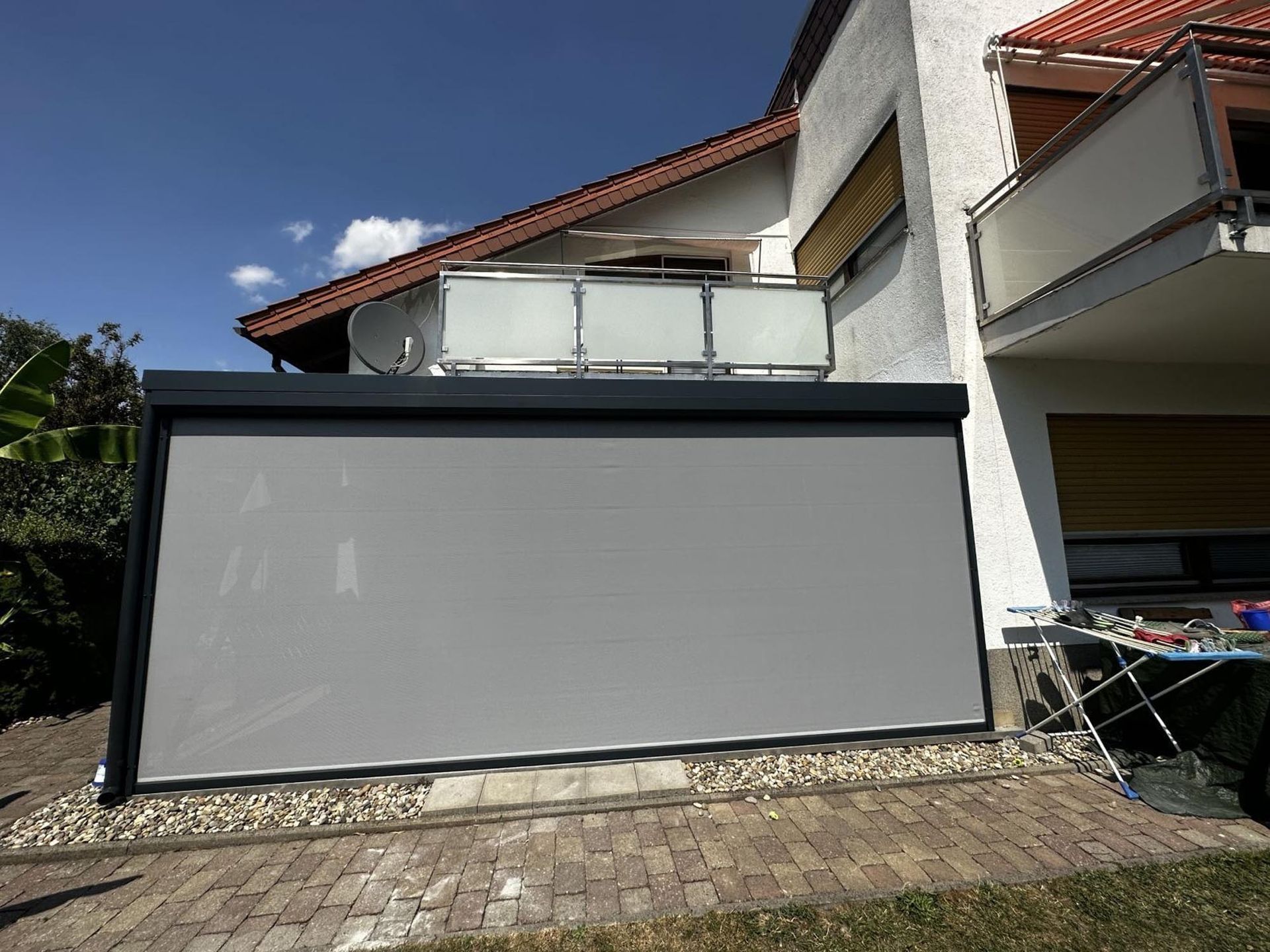 Große graue Outdoor-Projektionsleinwand neben einem Haus auf einer sonnigen Terrasse