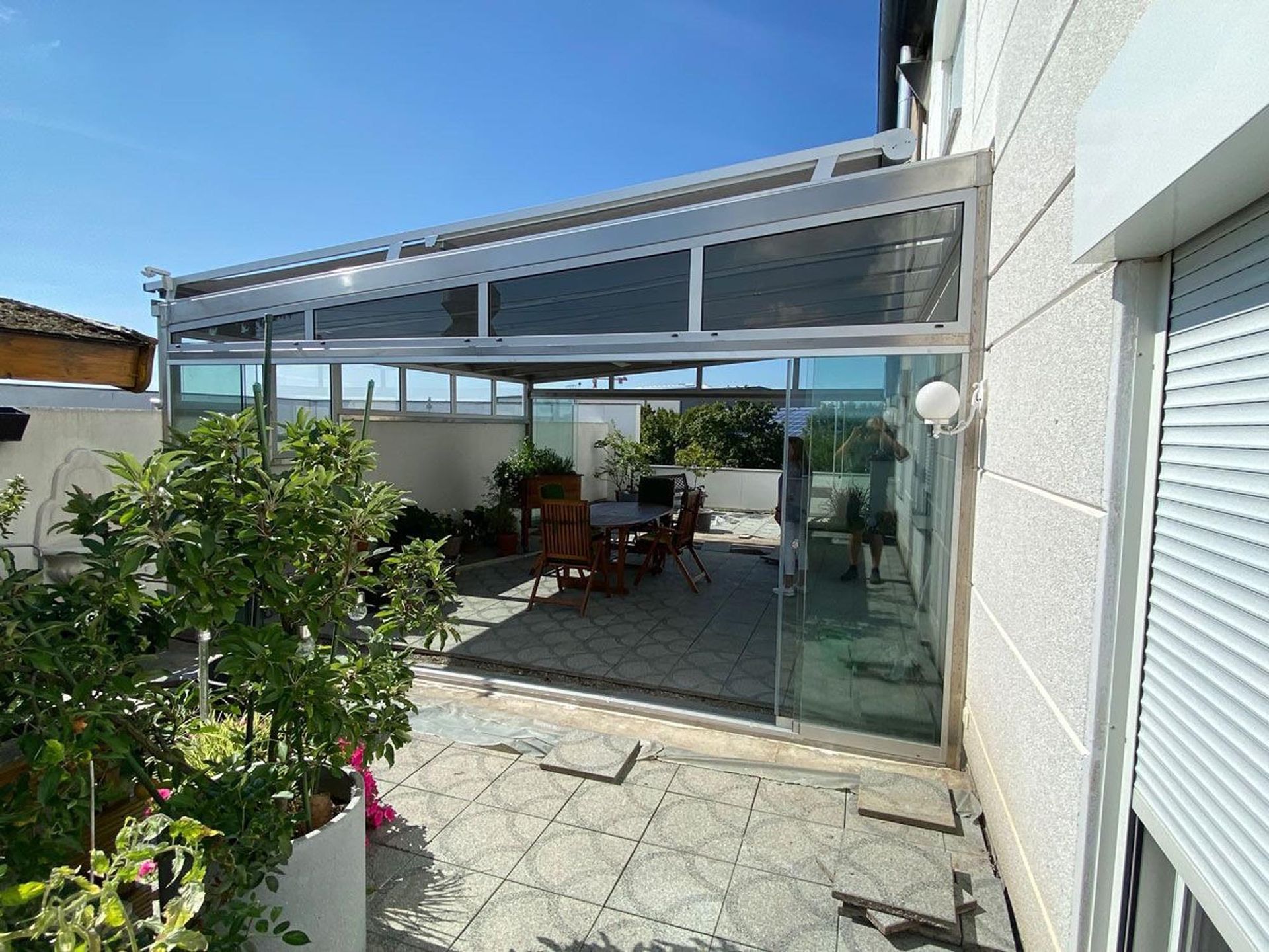 Terrasse mit Glasmarkise, Topfpflanzen, Esstisch im Freien und Glasschiebetüren neben einem Haus
