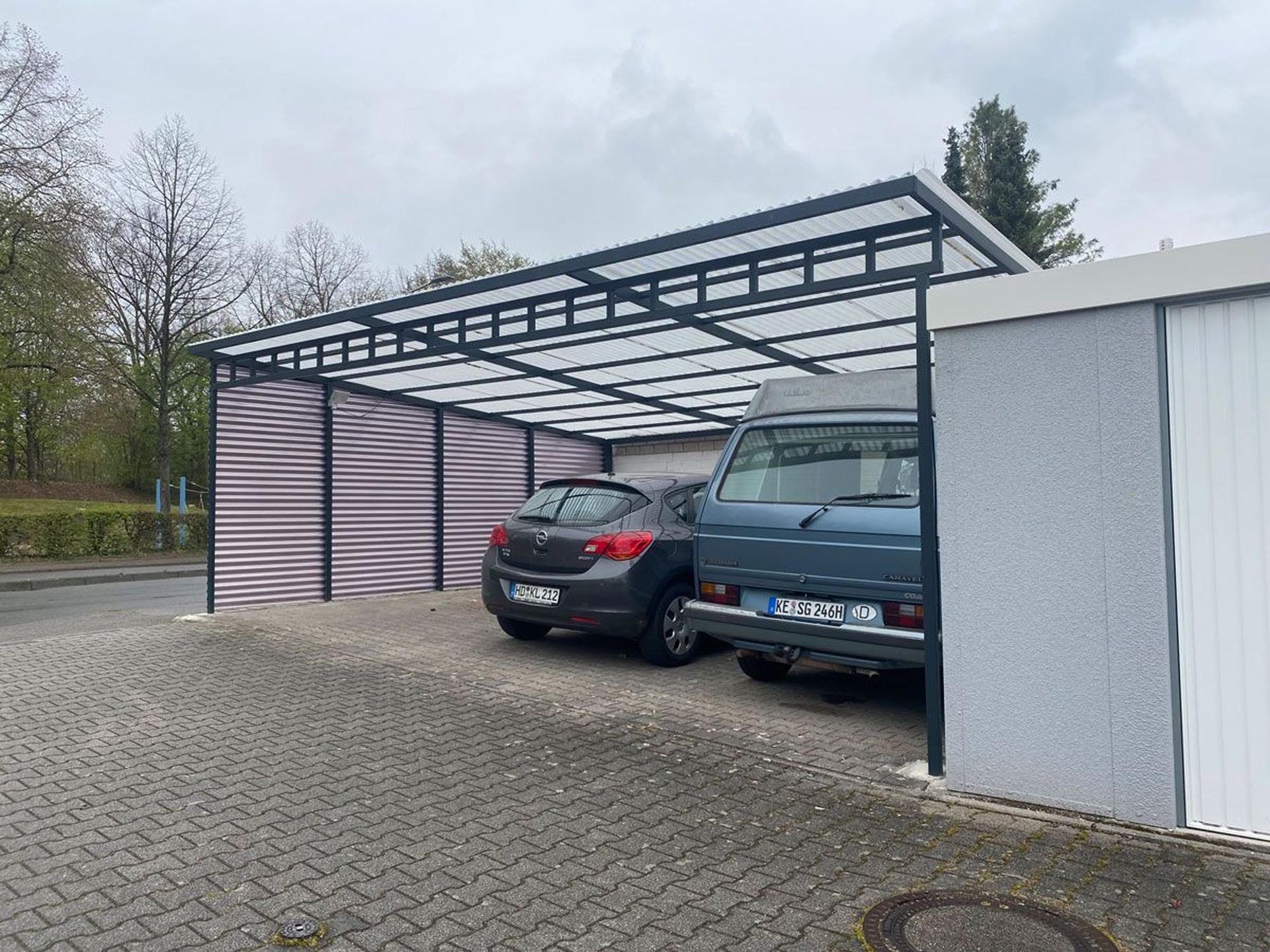 Zwei Autos parkten unter einem Carport aus Metall neben einem weißen Gebäude.