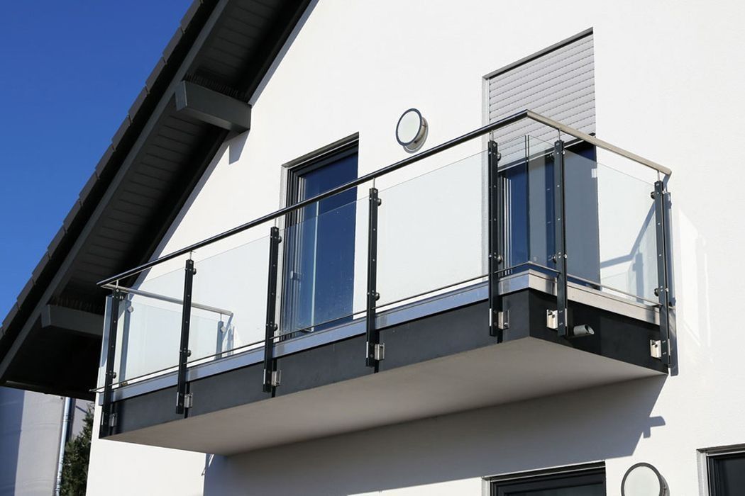Moderner weißer Hausbalkon mit Glasgeländer und blauen Flügeltüren
