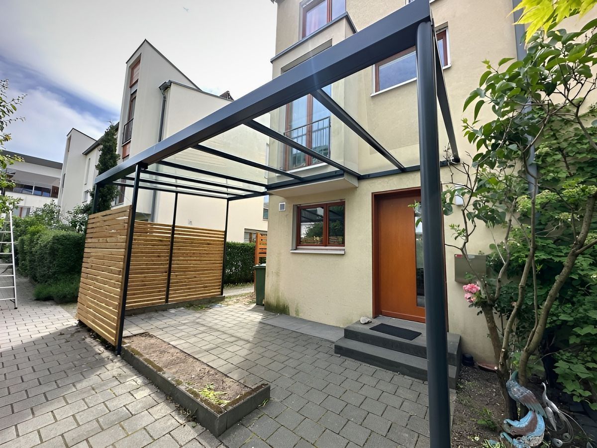 Moderner Hauseingang mit schwarzer Metallpergola, hölzernem Sichtschutz und orangefarbener Haustür