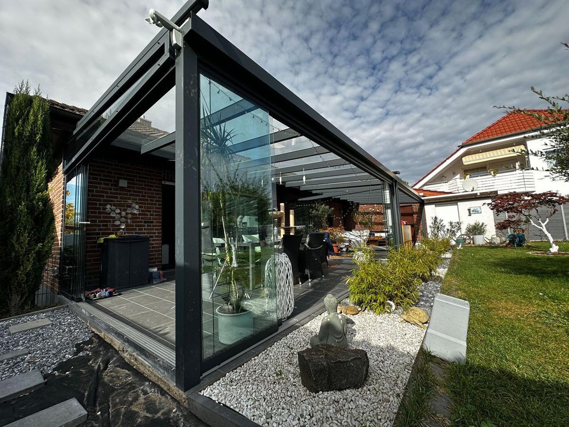 Moderner, verglaster Terrassenraum an einem Haus, mit schwarzem Rahmen und einem Garten davor