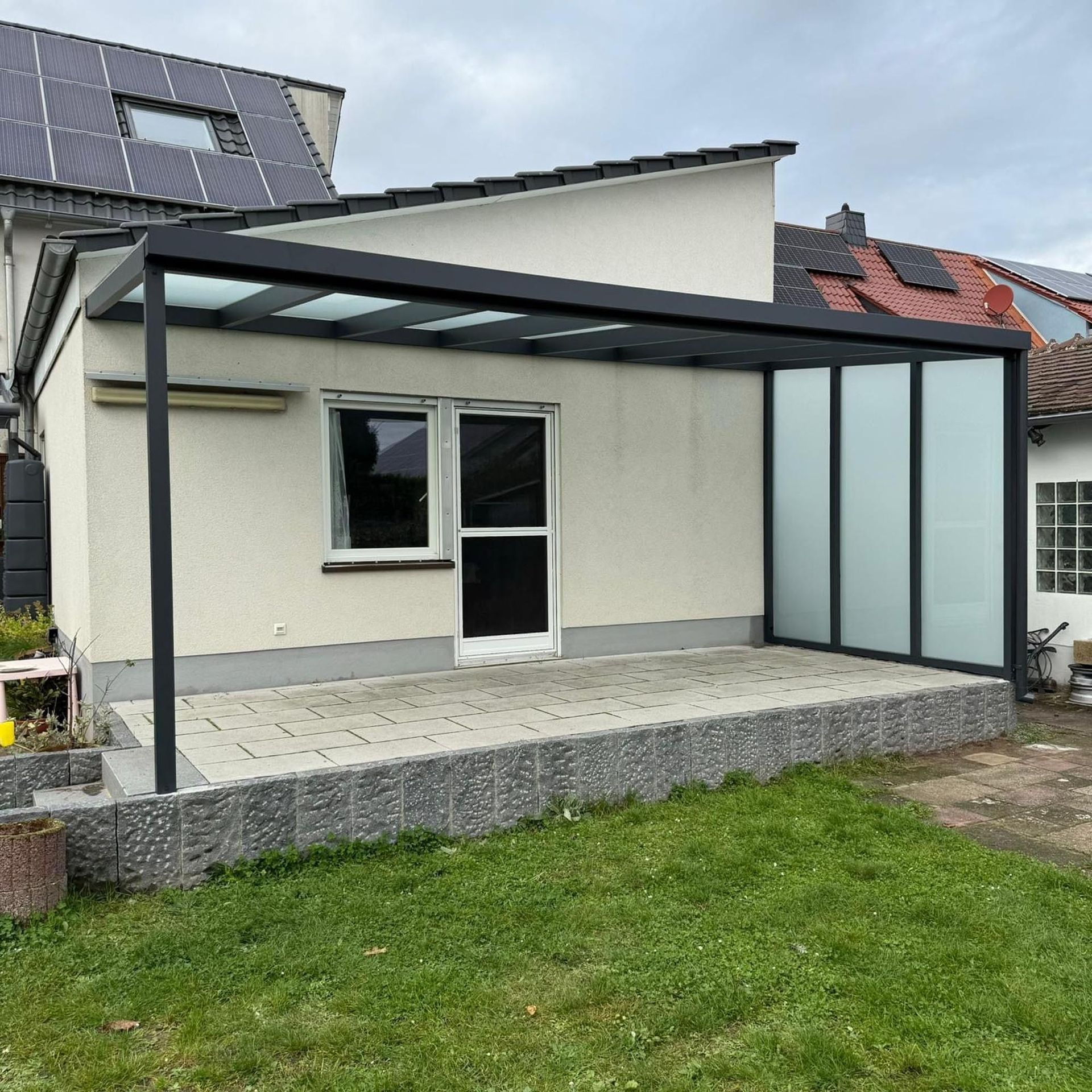 Moderner Hausanbau mit überdachter Terrasse, Milchglasscheiben und einem begrünten Hinterhof