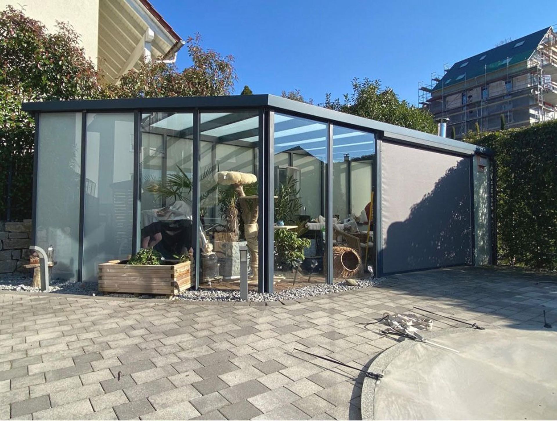 Ein verglaster Patio neben einer gepflasterten Auffahrt, in dem sich Pflanzen und nahegelegene Gebäude spiegeln.