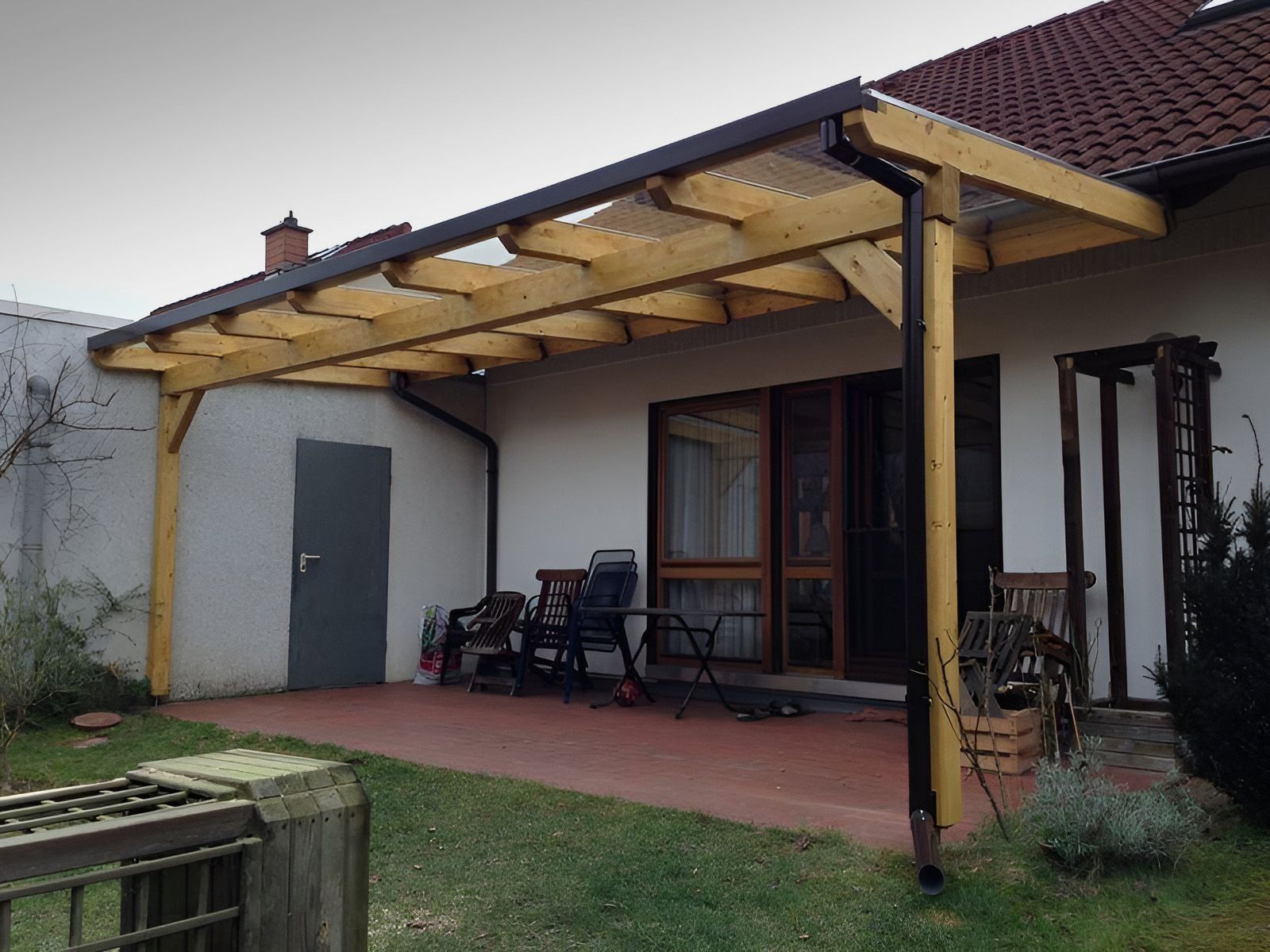 Überdachte Terrasse mit Holzdach, Gartenstühlen und einem Rasengarten neben einem weißen Haus