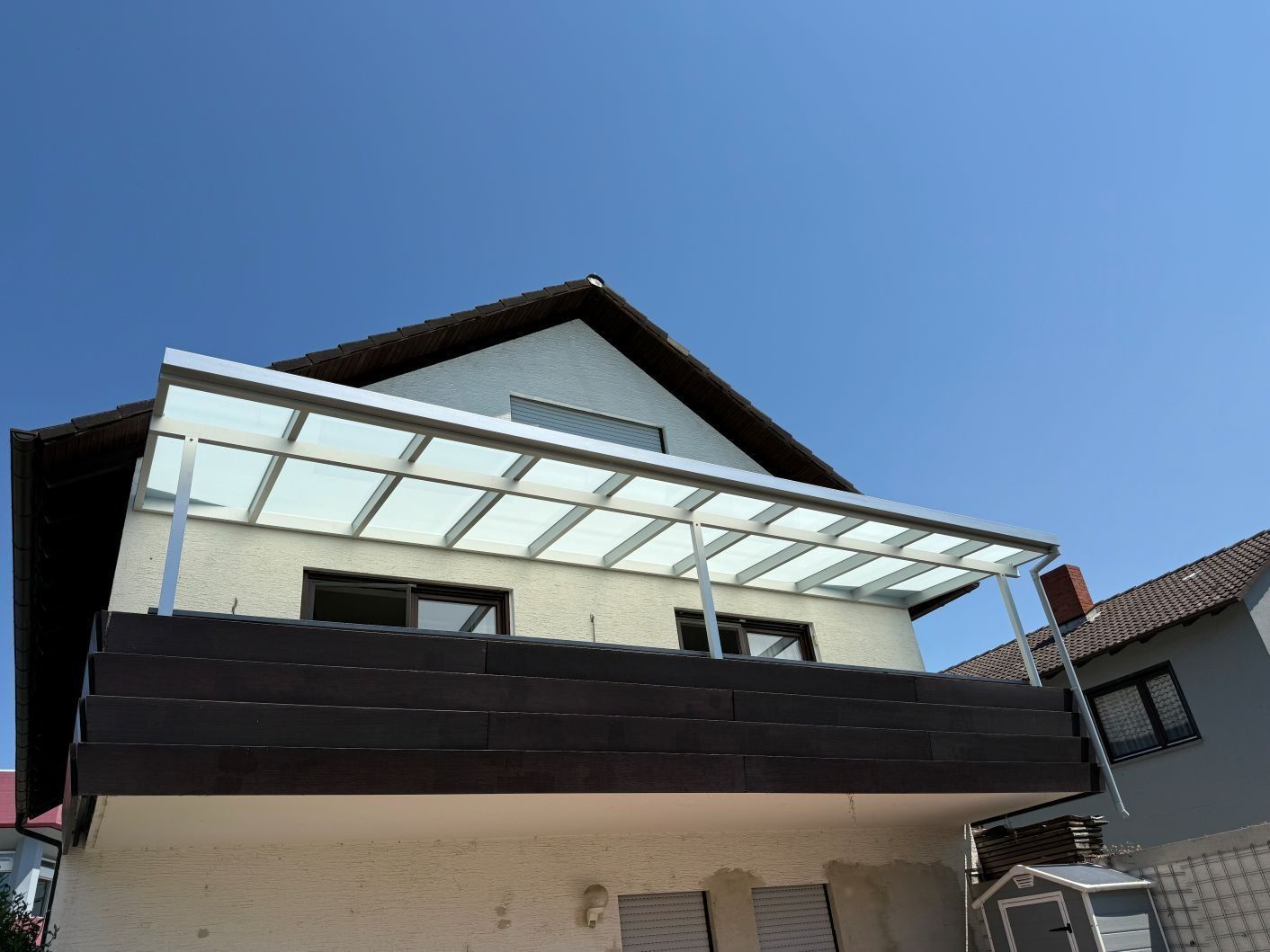 Modernes Haus mit dunklem Balkon und Glasmarkise vor blauem Himmel
