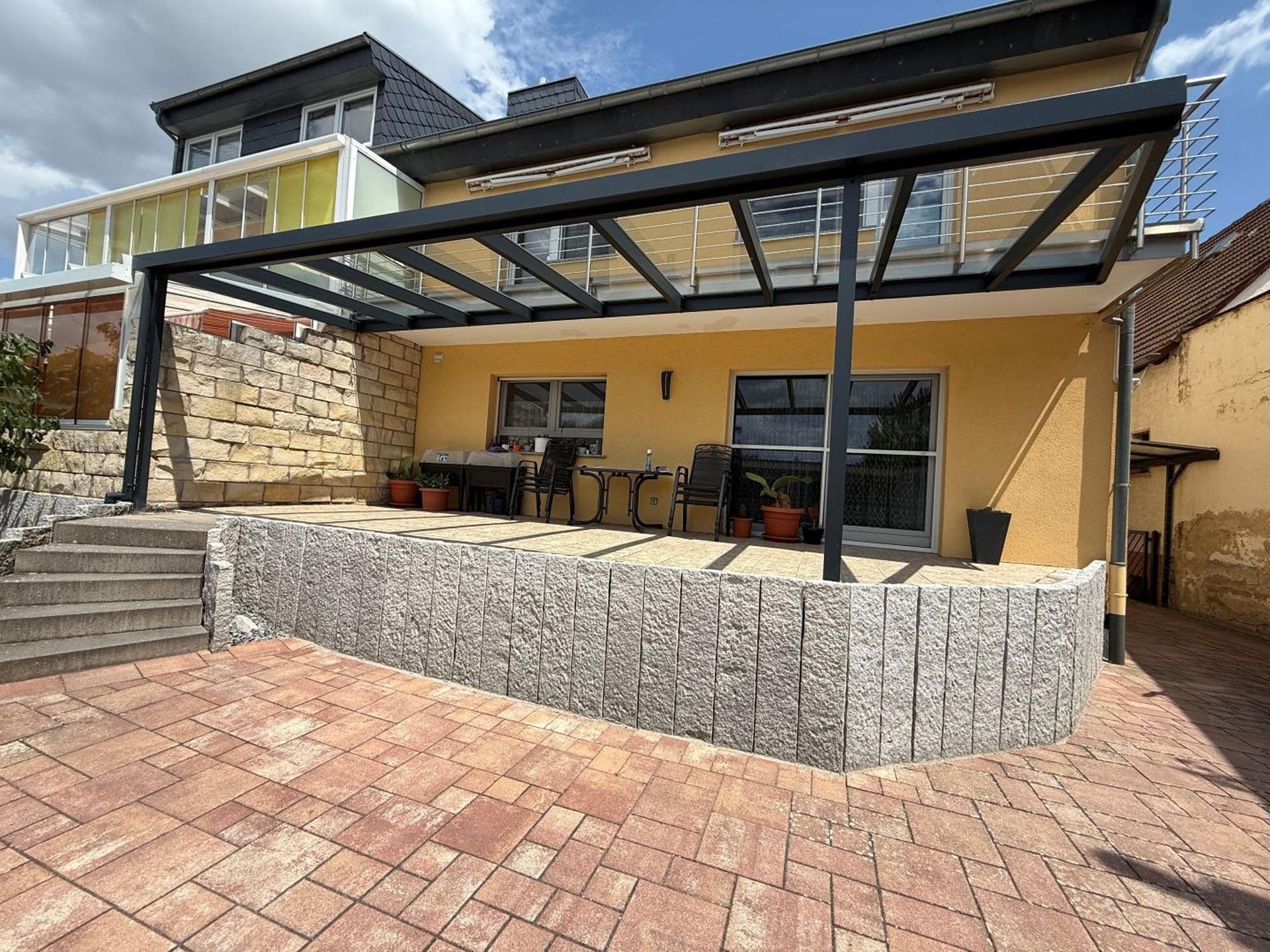 Hinterhof mit Pergola, Steinstufen und Sitzgelegenheiten im Freien vor einem gelben Haus