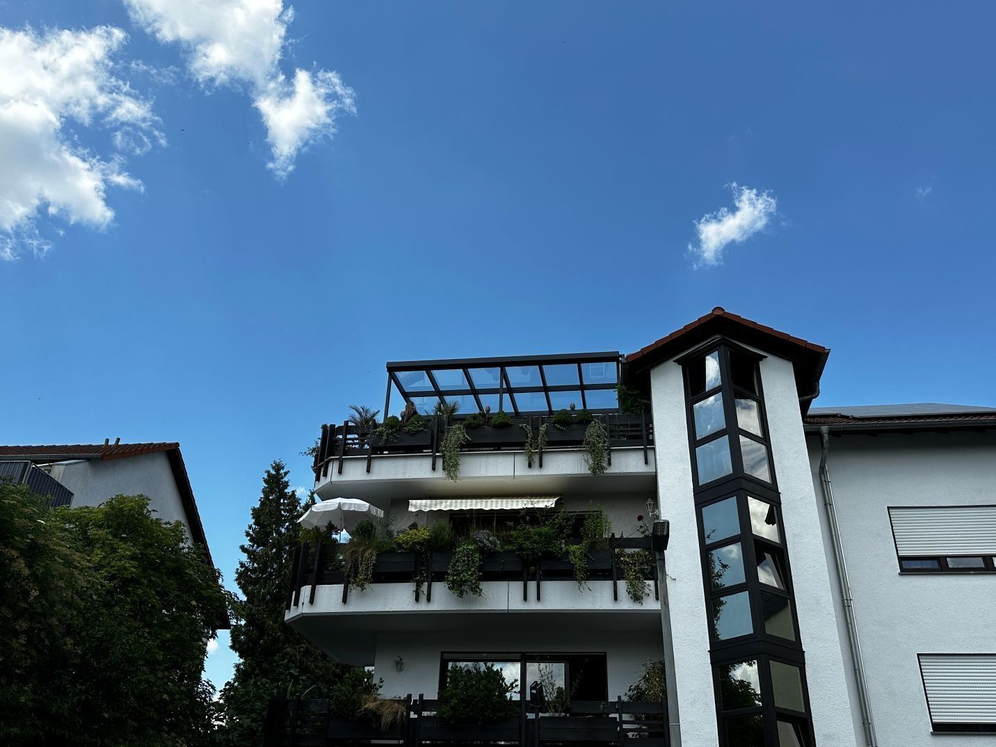 Modernes weißes Wohnhaus mit Balkonen und Pflanzen vor blauem Himmel