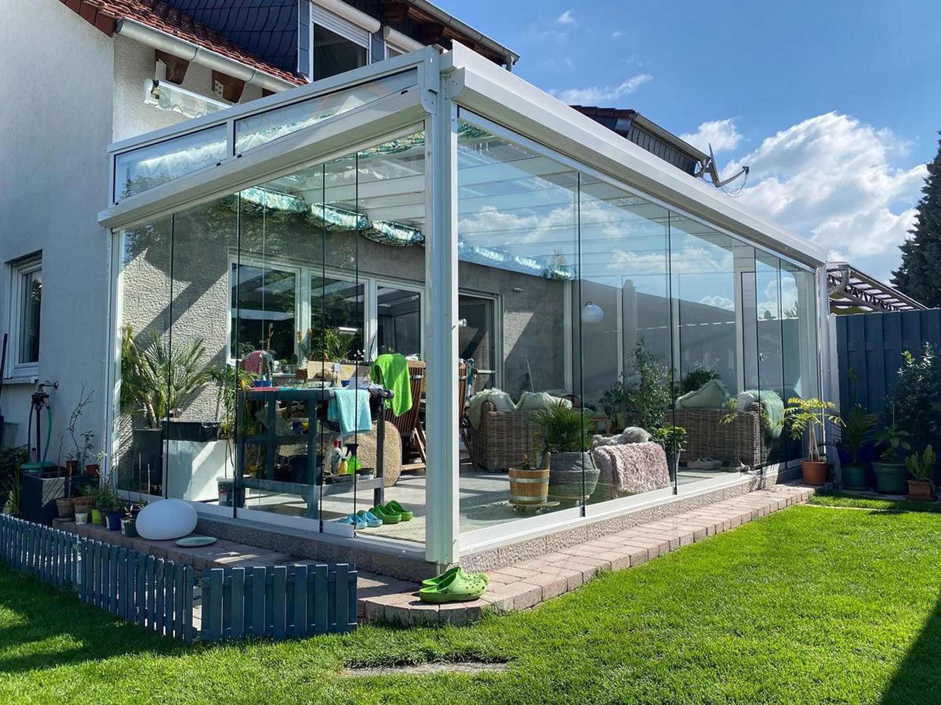 Verglaster Wintergartenanbau mit Pflanzen und Sitzgelegenheiten im Freien neben einem grünen Rasen