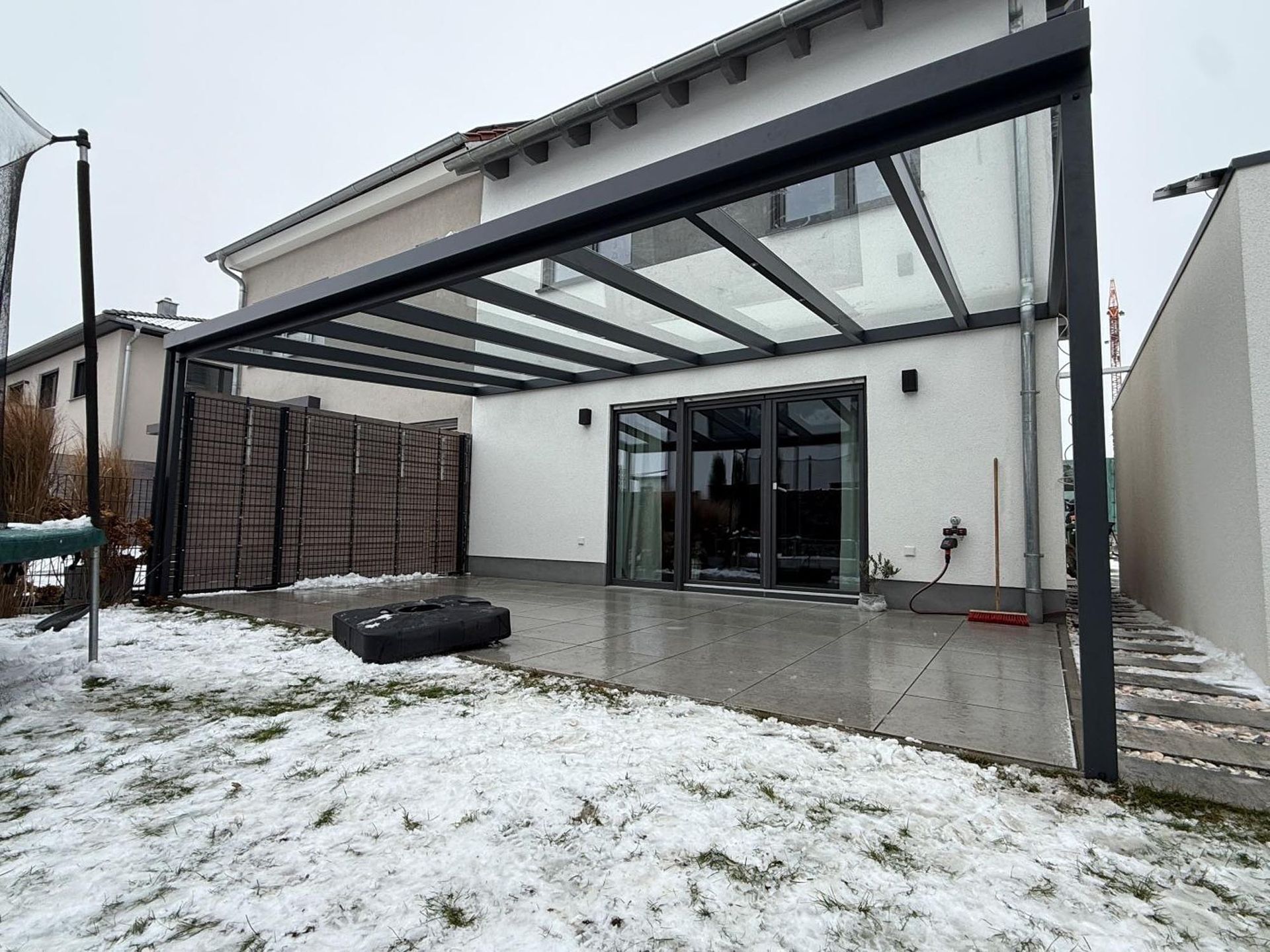 Verschneite Terrasse im Hinterhof mit moderner Glasdachpergola und Schiebetüren zu einem Haus