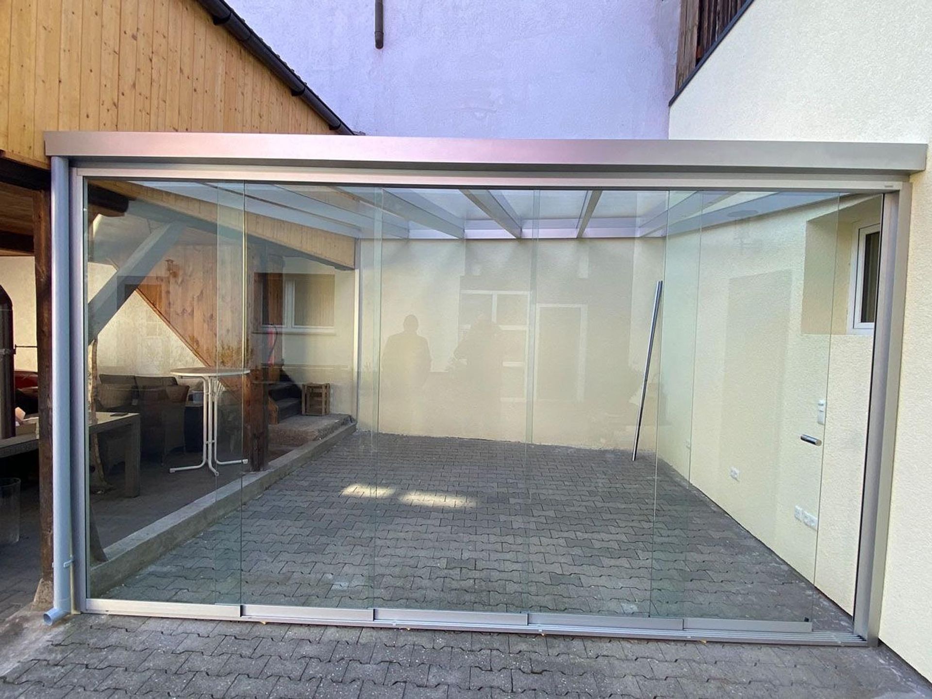 Überdachte Terrasse mit Klarglaswänden und gepflastertem Boden zwischen zwei Gebäuden