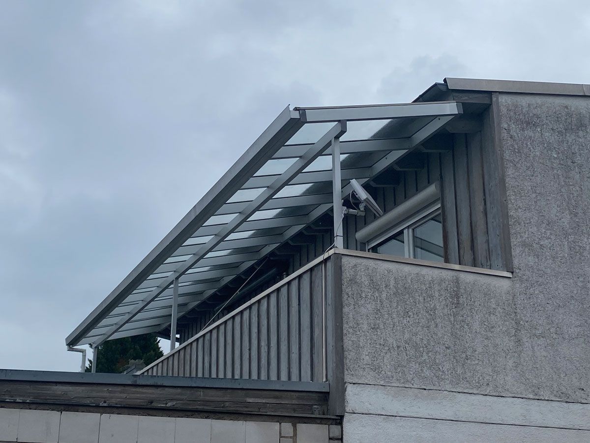 Graues Wohnhaus mit Metallmarkise und bewölktem Himmel