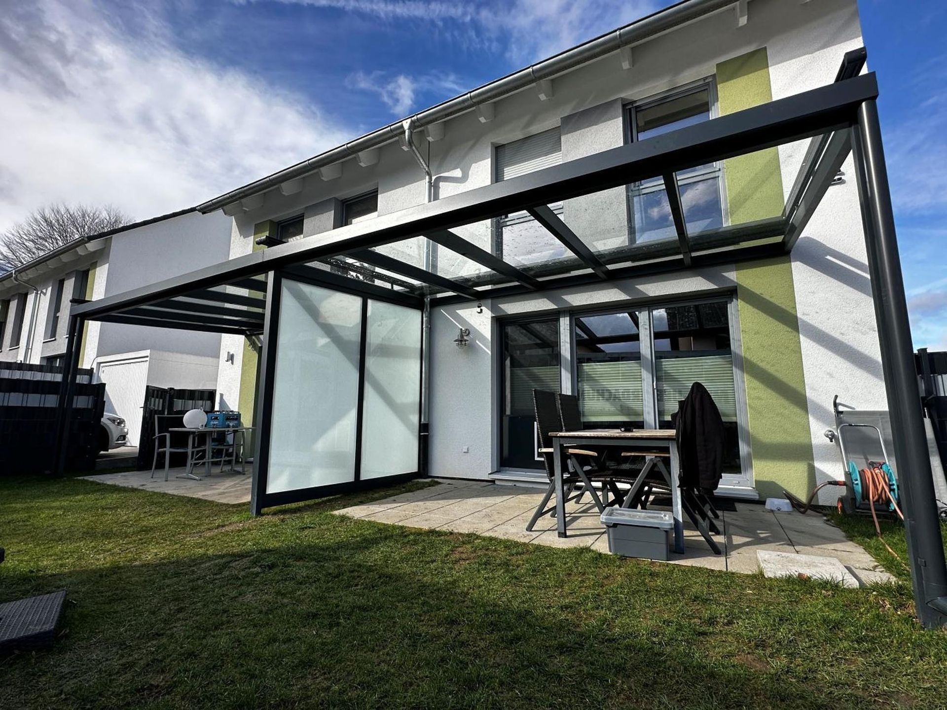 Moderne Glas-Terrassenpergola mit Esstisch im Freien neben einem Haus und einem Rasengarten