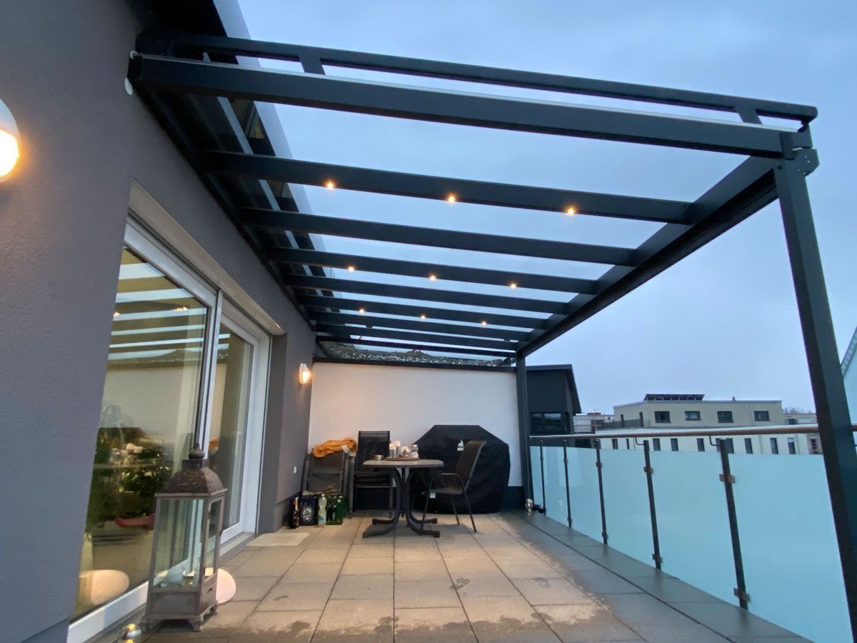 Dachterrasse mit Glasgeländer, Pergola, Lounge-Sitzgelegenheiten und Topfpflanzen in der Abenddämmerung
