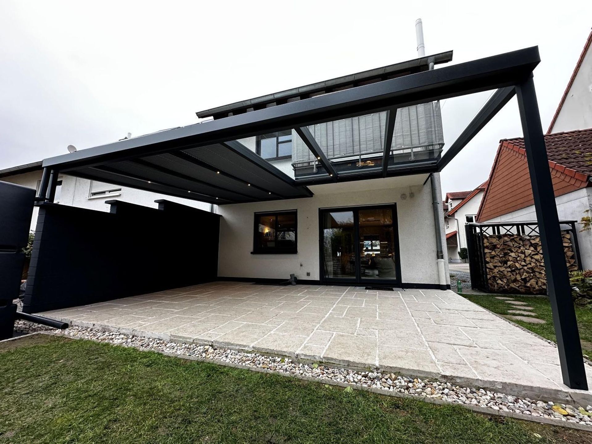 Moderne Hausterrasse mit schwarzer Metallpergola und gepflastertem Terrassenbereich