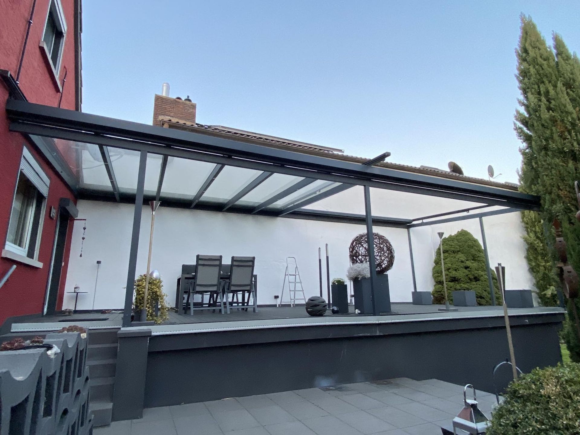 Moderne Terrasse mit Pergola, Essgruppe, Sitzgelegenheiten und Topfpflanzen neben einem Haus