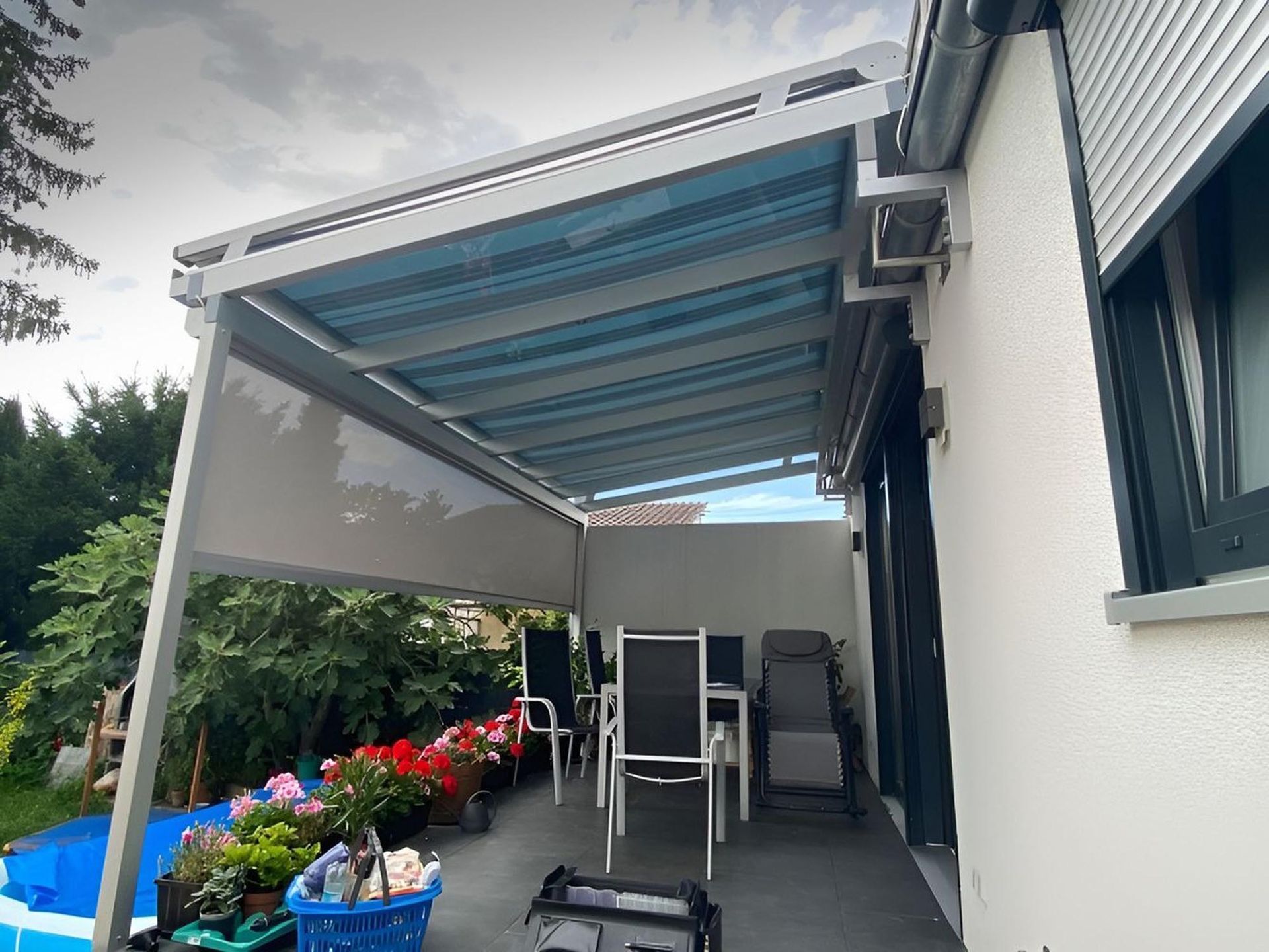 Überdachte Terrasse mit ausfahrbarer Markise, Gartenstühlen und Topfblumen neben einem Haus