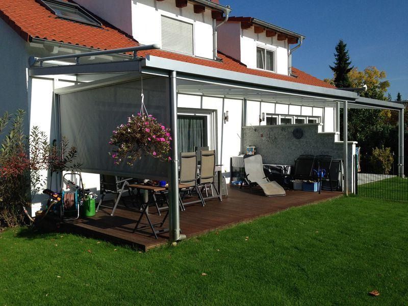Hinterhofterrasse mit weißer Pergola, Topfblumen, Gartenmöbeln und einem Haus mit rotem Dach dahinter