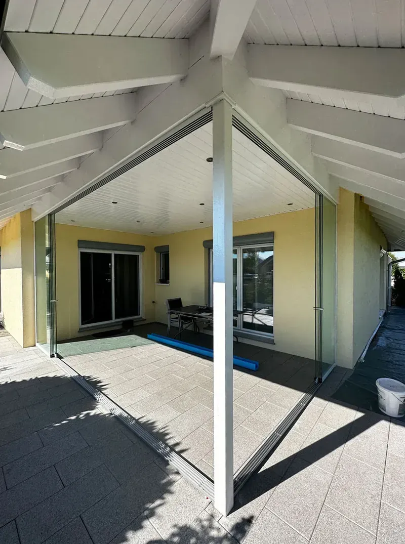 Überdachte Terrasse mit weißen Balken, gelben Wänden, Glasschiebetüren und Kiesboden.