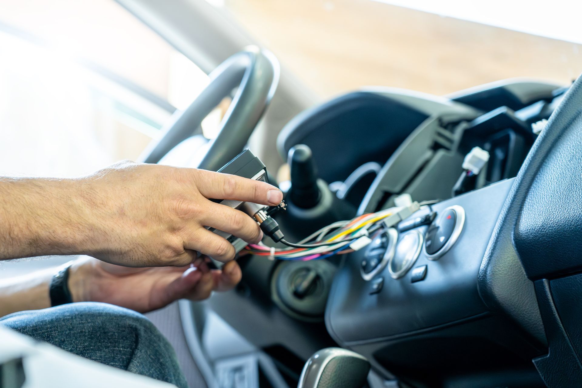 Des mains installent un autoradio et connectent les câbles au tableau de bord, près du volant.