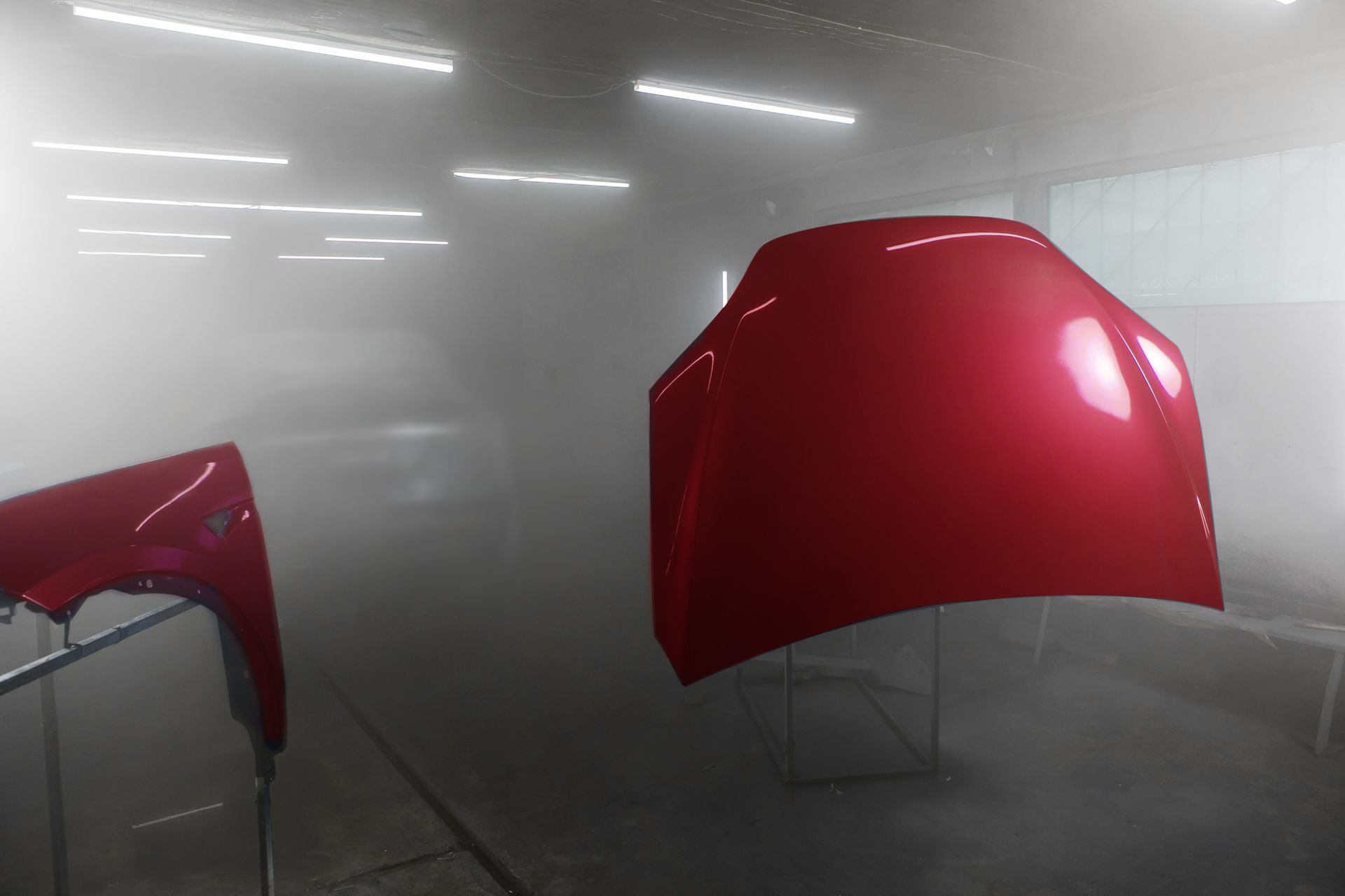 Capot et aile d'une voiture rouge dans une cabine de peinture.