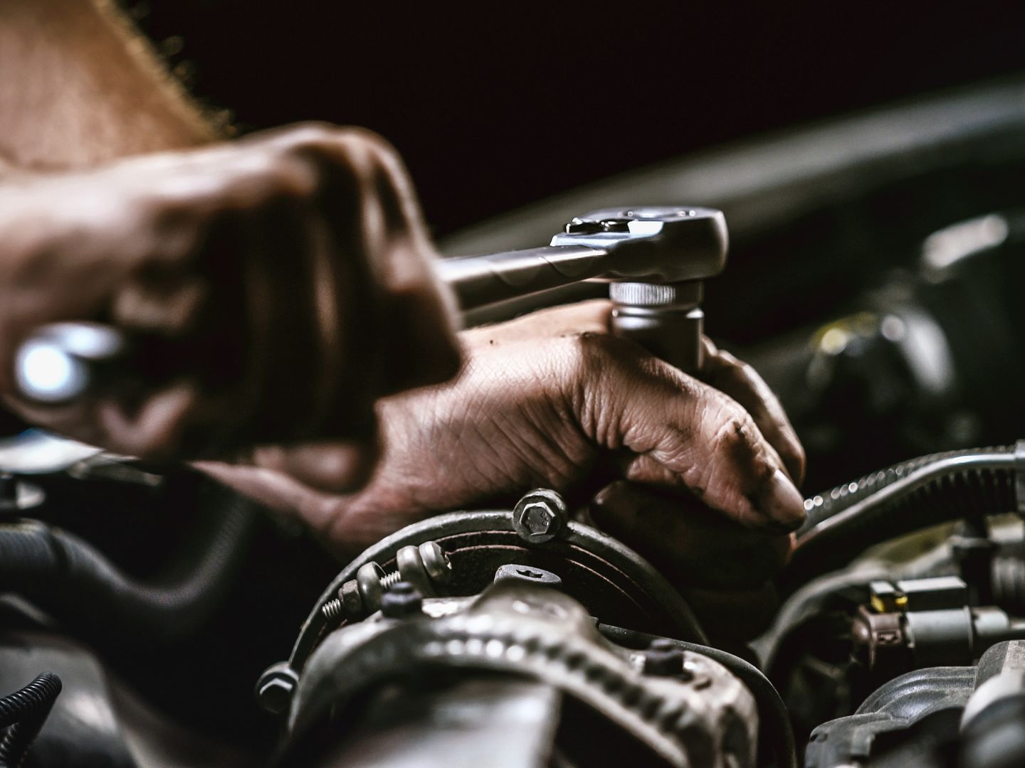 Les mains d'un mécanicien serrant un boulon avec une clé sur le moteur d'une voiture.