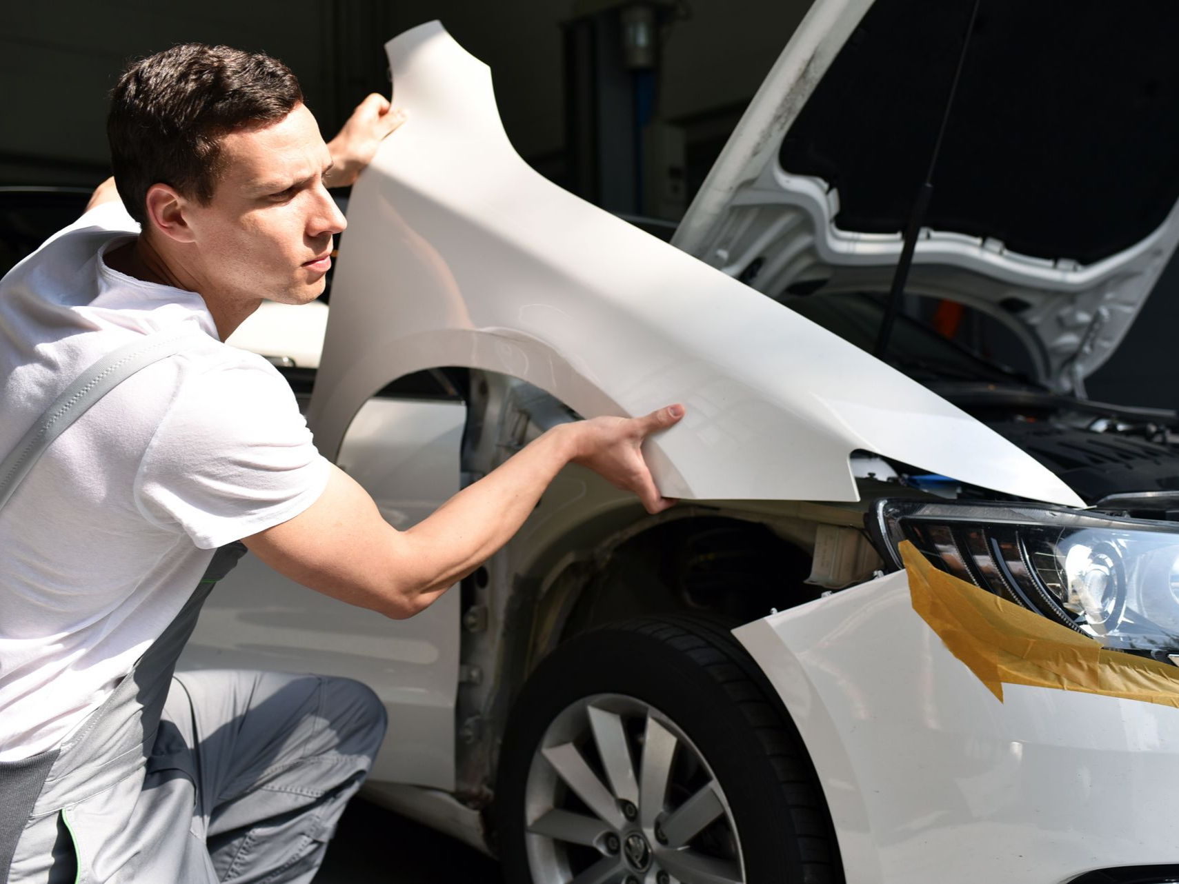 Un mécanicien installe une aile de voiture blanche sur un véhicule dans un atelier de réparation.