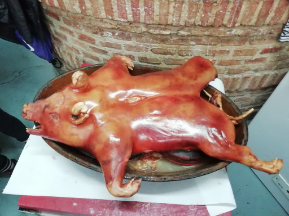 Cerdo entero asado en una bandeja de servir contra una pared de ladrillos.