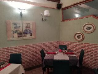 Pequeño comedor con mesa puesta, paredes rojas y blancas, cuadros enmarcados y un aplique de pared.