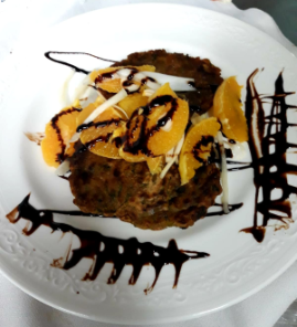 Postre servido en un plato blanco, decorado con rodajas de naranja y un chorrito de chocolate