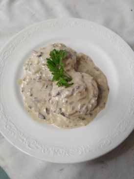 Salsa cremosa de champiñones sobre un plato blanco, adornada con una ramita de perejil.