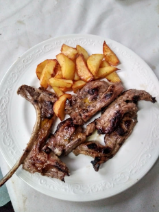 Plato con carne a la parrilla y patatas gajo doradas asadas sobre un plato blanco.